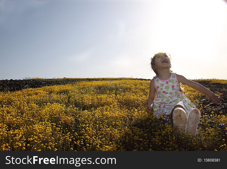 Little girl sitting in a yellow field of flowers looking up a the sky