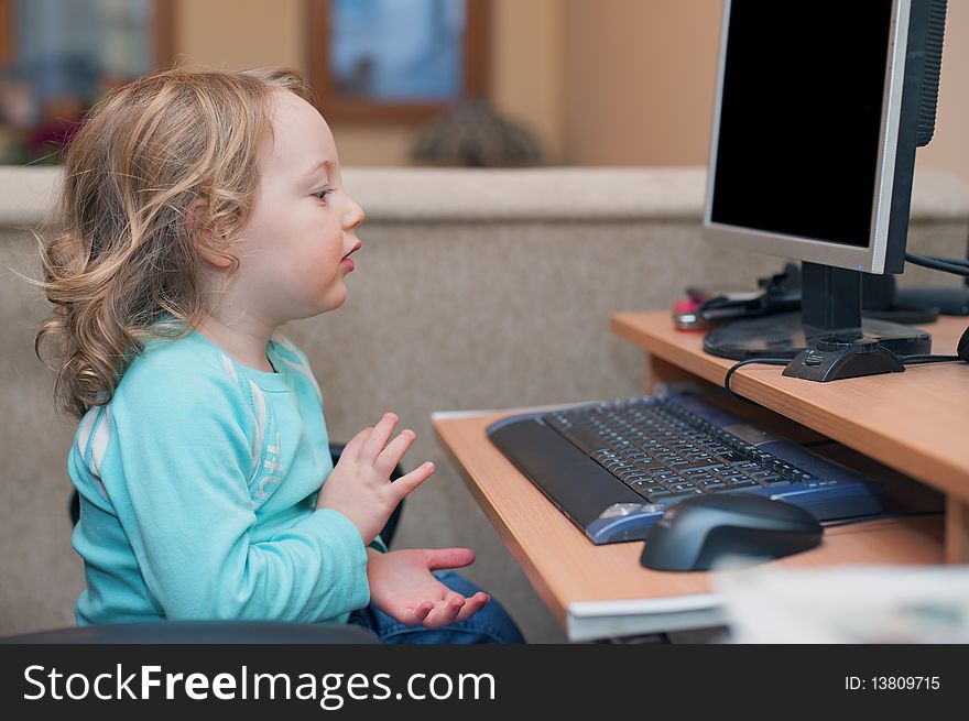 Little baby girl, sitting at a desktop computer at home, clapping hands with joy. Little baby girl, sitting at a desktop computer at home, clapping hands with joy