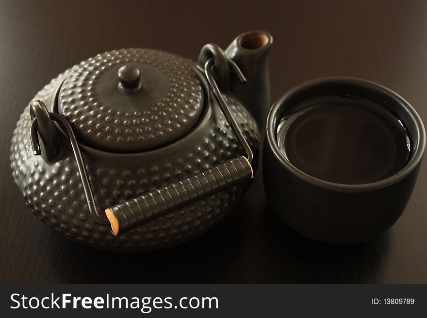 Black oriental teapot and cup on dark wooden background, selective focus. Black oriental teapot and cup on dark wooden background, selective focus