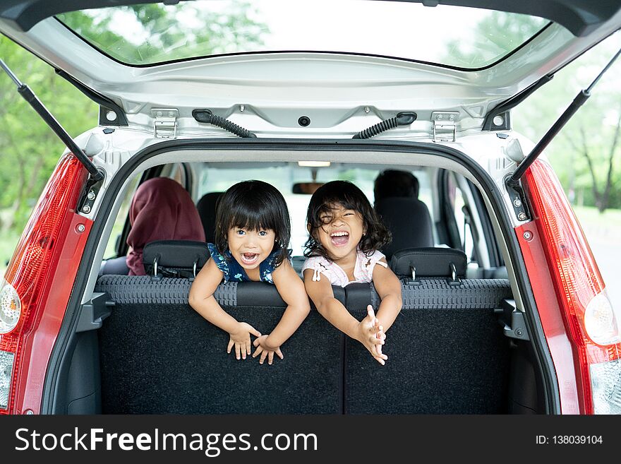 Two daughter playing in the car back seat and look back from baggage