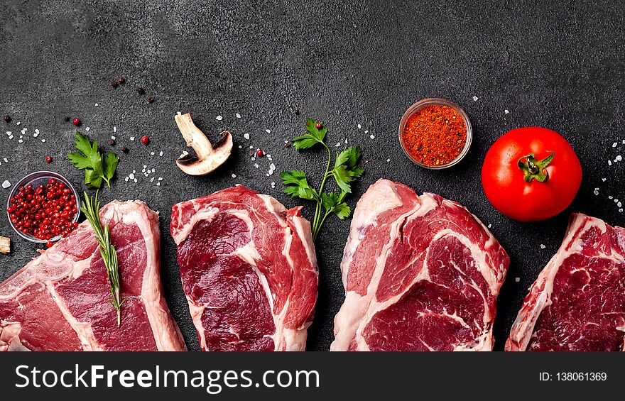 Meat raw steaks lie on black background with vegetables, tomatoes, marasmade, mushrooms. background image. top view