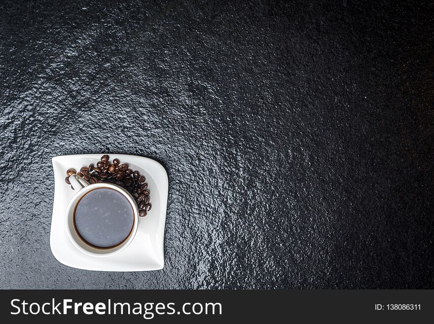 White cup of coffee and coffee beans on black stone table top view