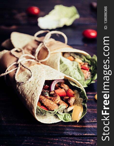 Traditional mexican tortilla wrap with vegetables and grilled chicken meat on dark wood table