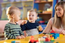 Babies Playing With Teacher In Kindergarten Or Nursery Stock Photos