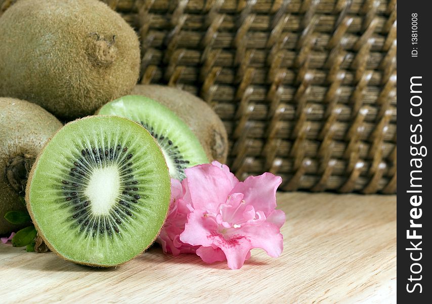 Cut kiwifruit on wood board with pink flower and wicker background