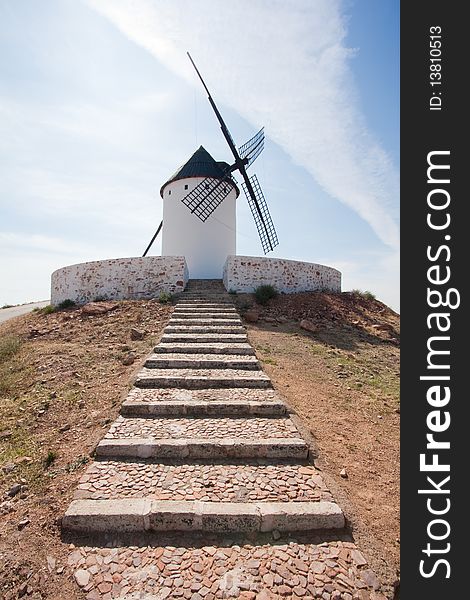 A lonely windmill standing at the end of some stairs, atop some hill.