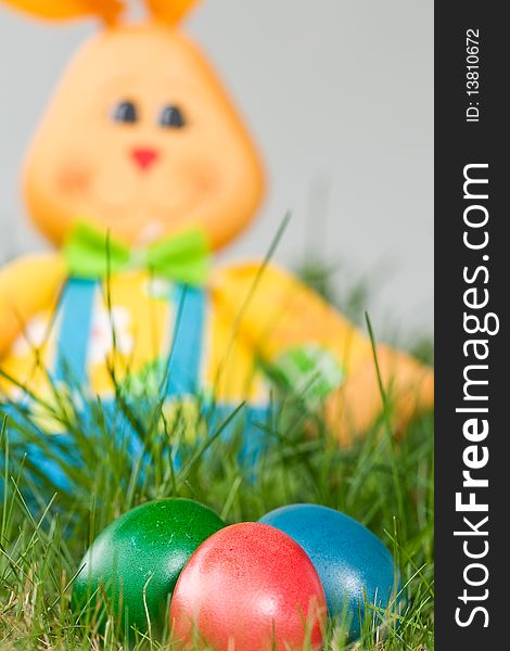 Toy easter bunny with colored eggs in the grass