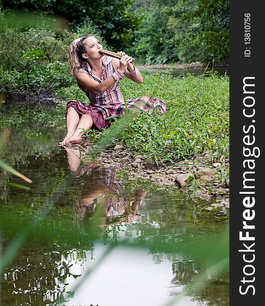 Beautiful young girl with fife playing near river