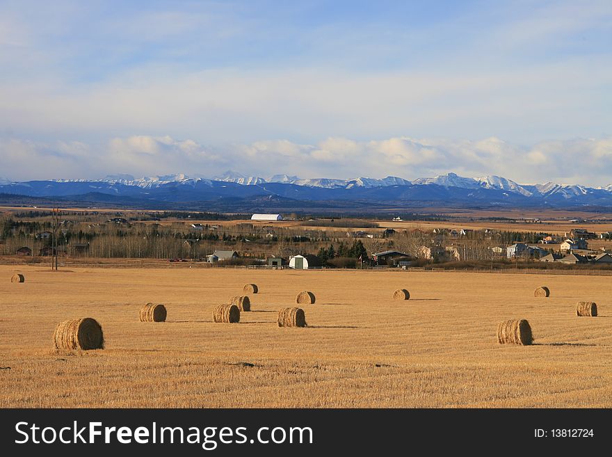 Farm near rocky mountains, with field, bales and fence in foreground. Farm near rocky mountains, with field, bales and fence in foreground