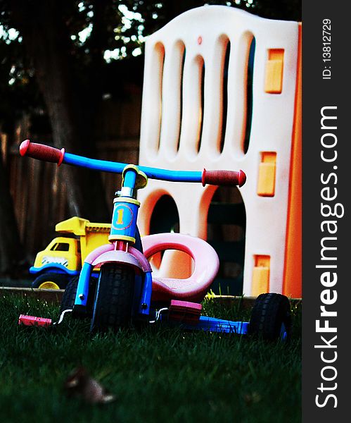 Tricycle with faded colors in a backyard with other toys in the background. Tricycle with faded colors in a backyard with other toys in the background.