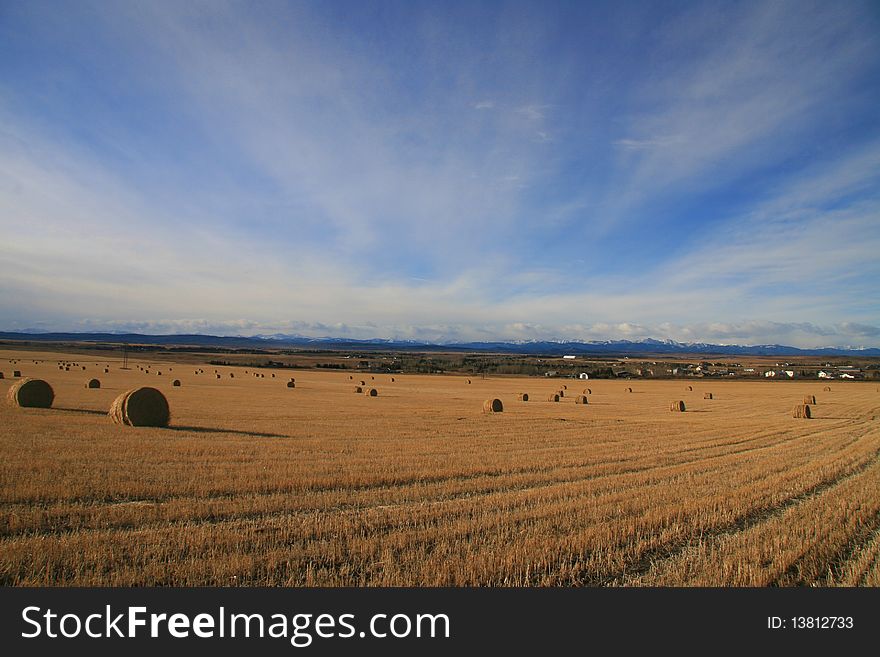 Farm near rocky mountains, with field, bales and fence in foreground. Farm near rocky mountains, with field, bales and fence in foreground