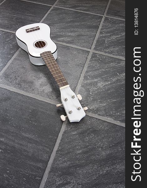 A white ukulele on a black/grey slate floor. A white ukulele on a black/grey slate floor.