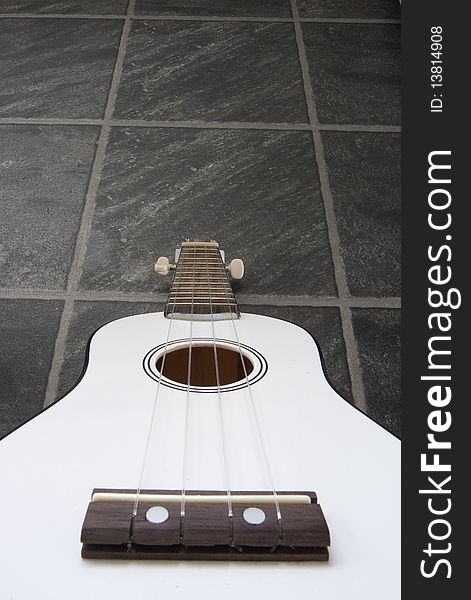 A white ukulele against a black/grey slate floor background. A white ukulele against a black/grey slate floor background.