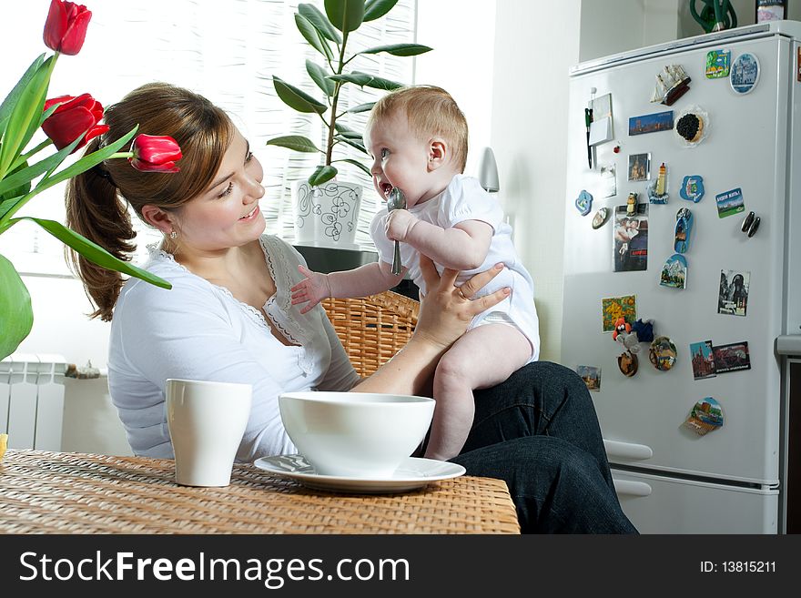 Young beautiful mother feeding her litlle cute baby daughter at the kitchen. Young beautiful mother feeding her litlle cute baby daughter at the kitchen