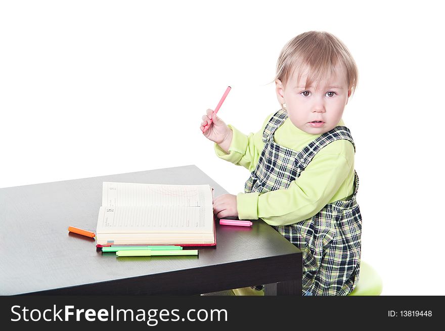 The little girl sits at a table and does a homework, draws in a notebook. It is isolated on a white background. The little girl sits at a table and does a homework, draws in a notebook. It is isolated on a white background