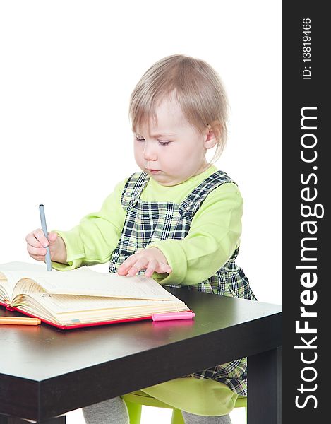 The little girl sits at a table and does a homework, draws in a notebook. It is isolated on a white background. The little girl sits at a table and does a homework, draws in a notebook. It is isolated on a white background