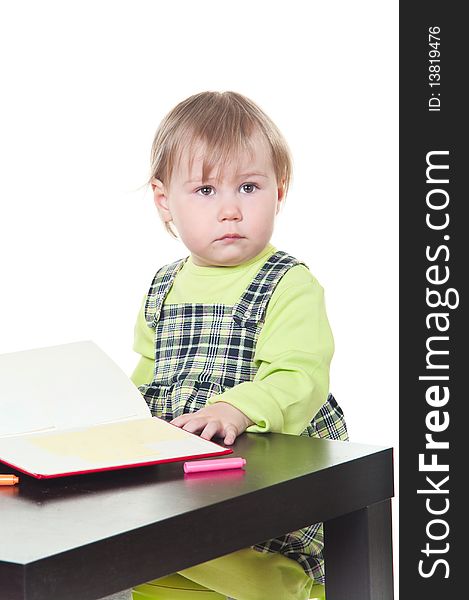 The little girl sits at a table and does a homework, draws in a notebook. It is isolated on a white background. The little girl sits at a table and does a homework, draws in a notebook. It is isolated on a white background