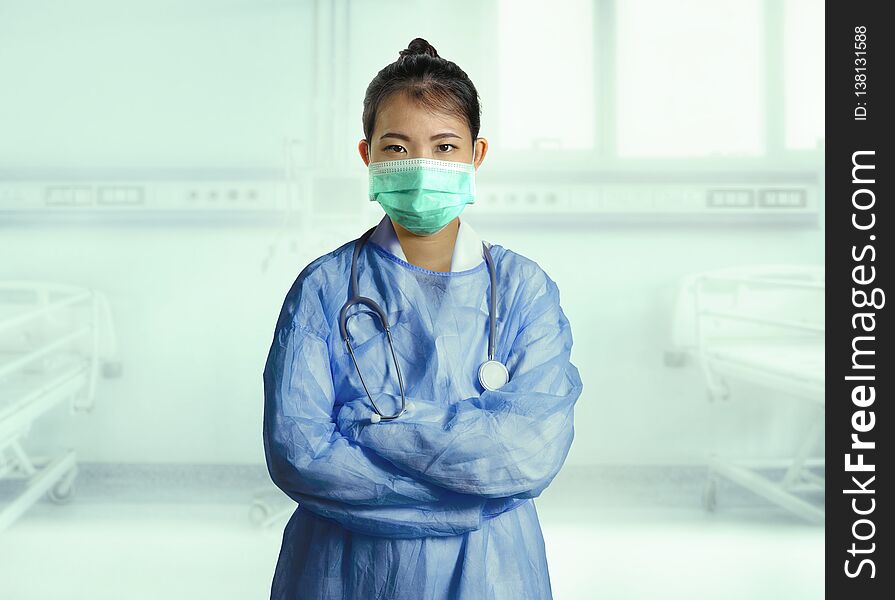 Confident and successful Asian Korean medicine doctor woman in hospital scrubs and mask posing at clinic patient bed in