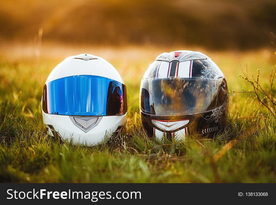 Two motorcycle helmets lie on the grass in the sun