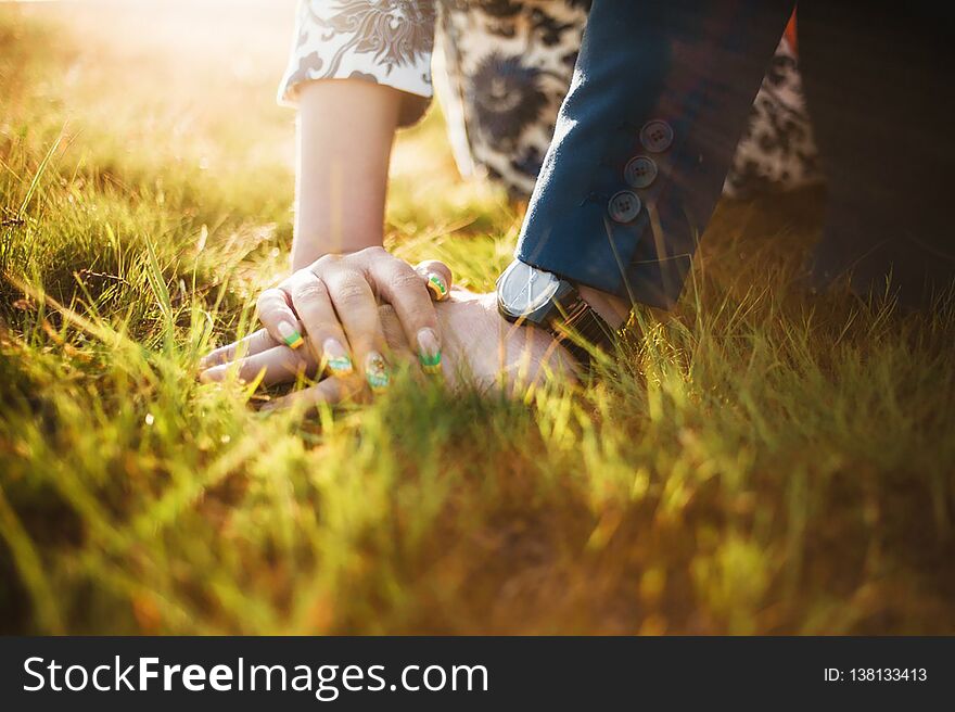 Lovers sit embracing on the grass in the sun, she gently put her hand on his palm