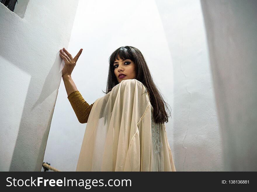 Portrait Beautiful Moroccan Girl in white mantle cloak in tight white stairs passage of Picturesque Dar Si Said Riyad in