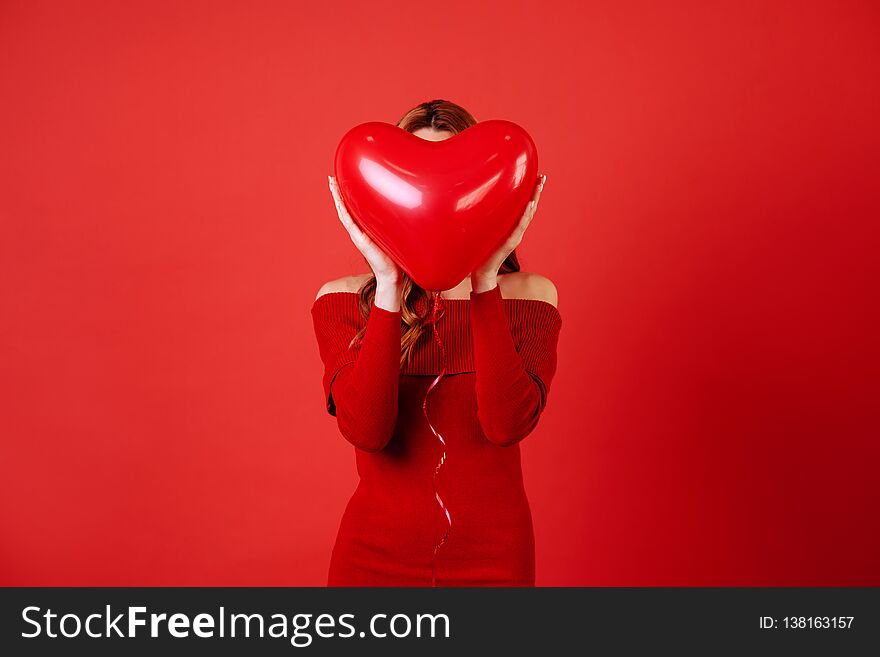 Young charming girl with long blonde curly hair, in red dress holding air balloons, posing at camera. St. Valentine`s day. Young charming girl with long blonde curly hair, in red dress holding air balloons, posing at camera. St. Valentine`s day.