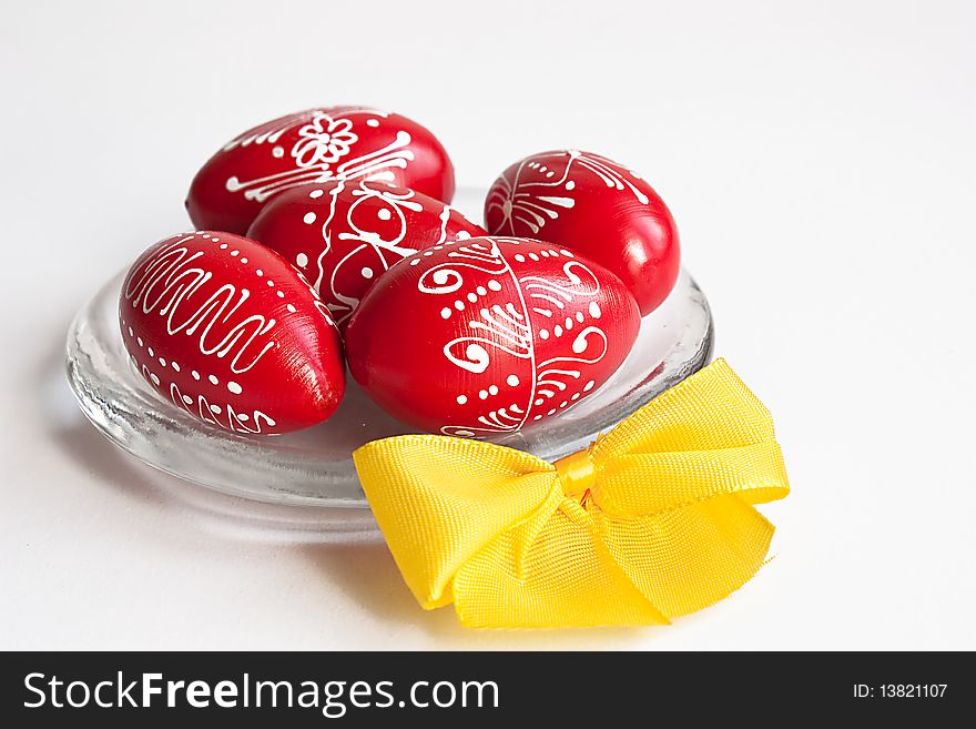 Red Easter eggs on a glass plate with yellow ribbon on white background. Red Easter eggs on a glass plate with yellow ribbon on white background