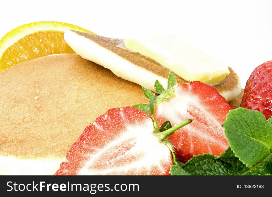 Stack of pancakes with butter, strawberries, orange quarters and mint leaves