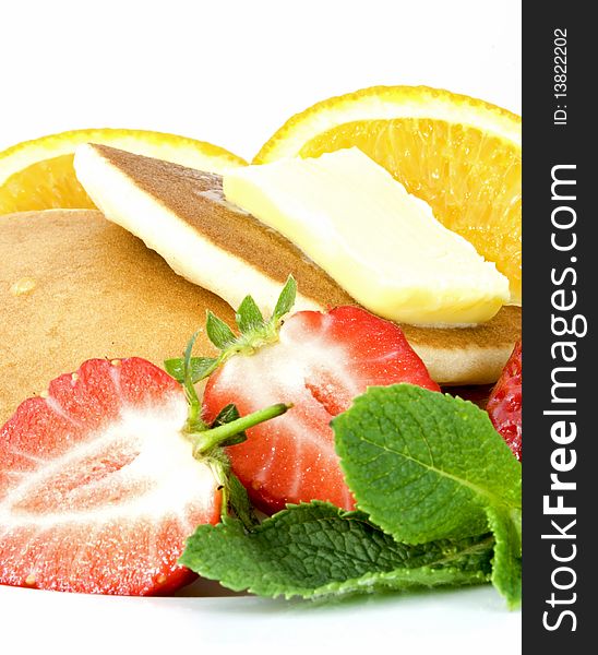 Stack of pancakes with butter, strawberries, orange quarters and mint leaves