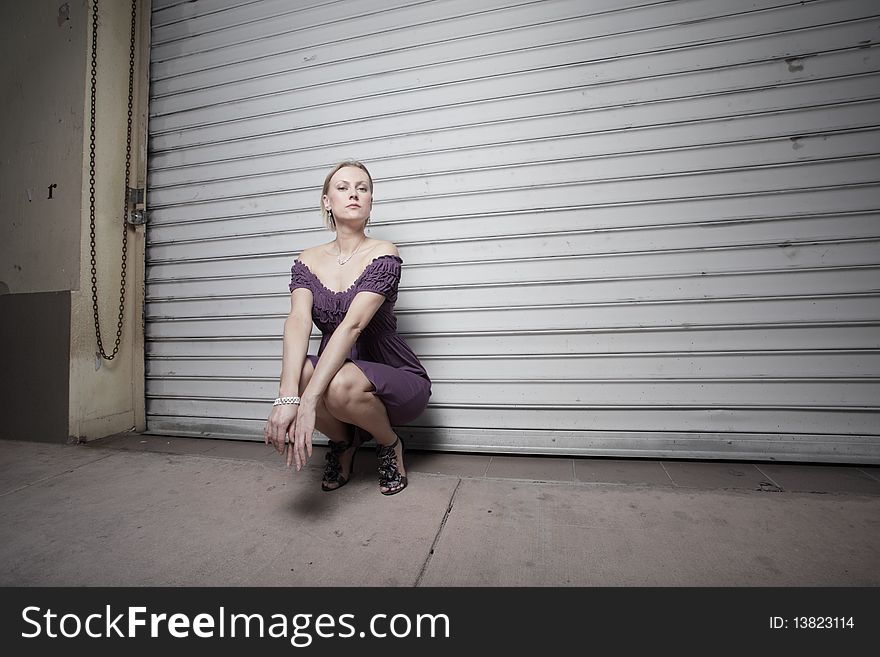 Attractive young woman squatting in an urban setting at night. Attractive young woman squatting in an urban setting at night