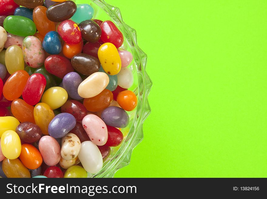 Pastel and bright jelly beans in a glass dish, against a bright green background. Pastel and bright jelly beans in a glass dish, against a bright green background