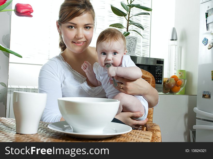 Young beautiful mother feeding her litlle cute baby daughter at the kitchen. Young beautiful mother feeding her litlle cute baby daughter at the kitchen