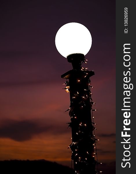 A white-light lamp decorated with light bulbs in front of a sunset background. A white-light lamp decorated with light bulbs in front of a sunset background