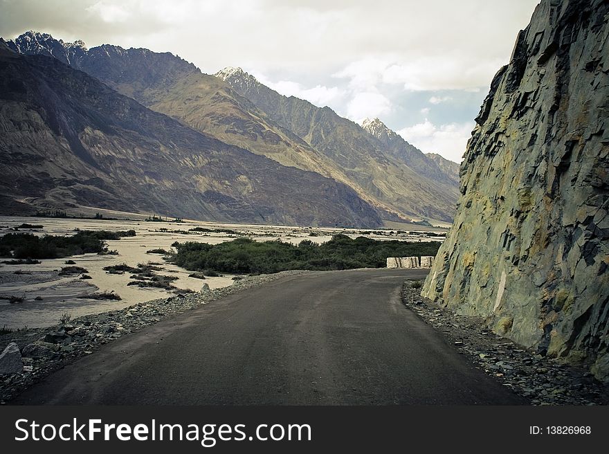 Blind curve on mountain road in Himalaya. Kashmir, India. Mountain range on background.