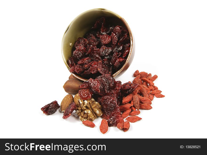 Red ripe dried cranberries spilling from a small bowl with mixed nuts and goji berries on a reflective white background. Red ripe dried cranberries spilling from a small bowl with mixed nuts and goji berries on a reflective white background