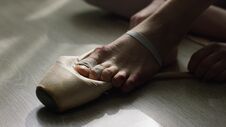 Close-up Of Ballerina`s Feet. Ballerina Preparing For Training, And Tying Ribbon Of Pointe Shoes Sitting On Floor In Royalty Free Stock Image