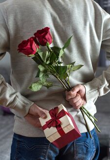 Young Man Holding Red Rose Flowers And Gift Box Behind His Back At Home Royalty Free Stock Image