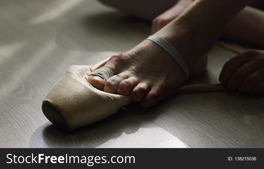 Close-up Of Ballerina`s Feet. Ballerina Preparing For Training, And Tying Ribbon Of Pointe Shoes Sitting On Floor In