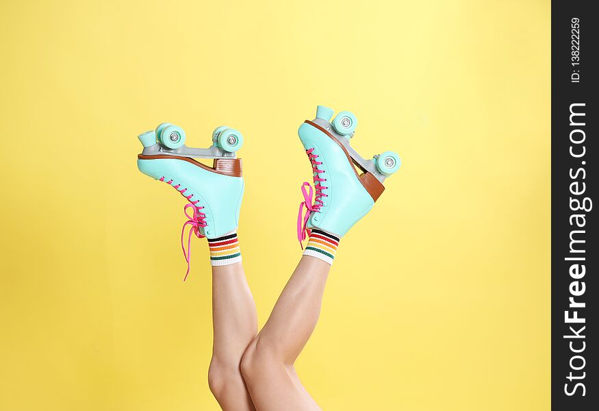 Young woman with retro roller skates on color background, closeup