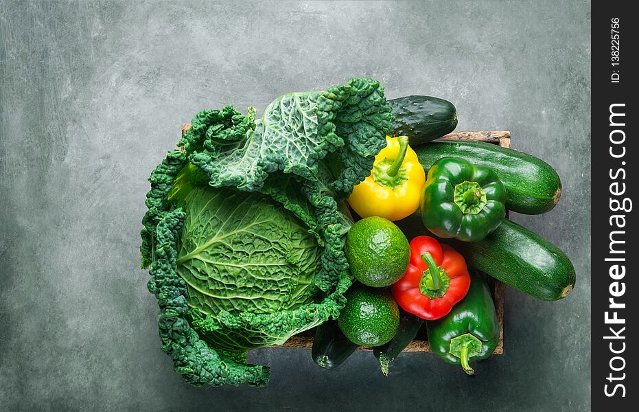 Assortment of organic green red yellow raw vegetables savoy cabbage cucumbers zucchini avocado capsicums in wood box