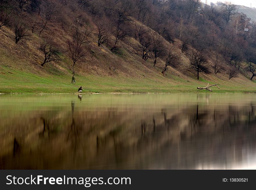 Fisher on a river bank (with view of mirroring trees)