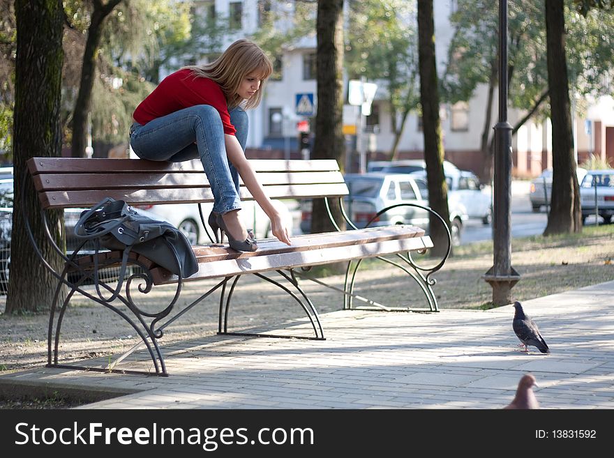 A beautiful girl sits on the back of bench and feeds a pigeon. A beautiful girl sits on the back of bench and feeds a pigeon.