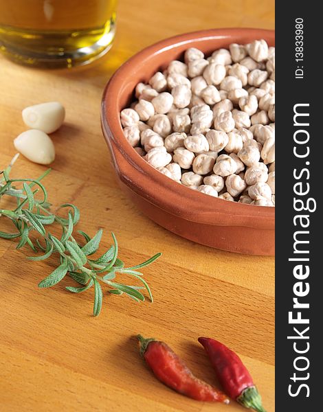 A bowl of raw chickpeas, with olive oil, garlic, chilli peppers and fresh rosemary on a wooden board. A bowl of raw chickpeas, with olive oil, garlic, chilli peppers and fresh rosemary on a wooden board