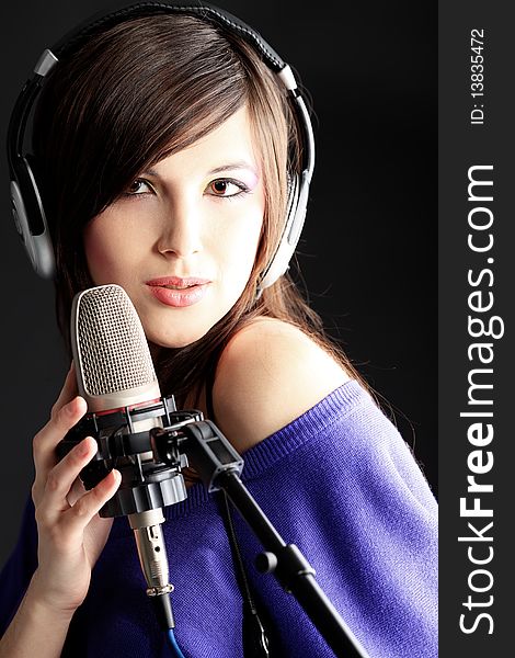 Shot of a pretty young woman in headphones singing a song with a microphone. Shot in a studio. Shot of a pretty young woman in headphones singing a song with a microphone. Shot in a studio.