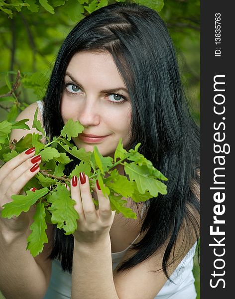 Young woman in forest touches oak leaves.