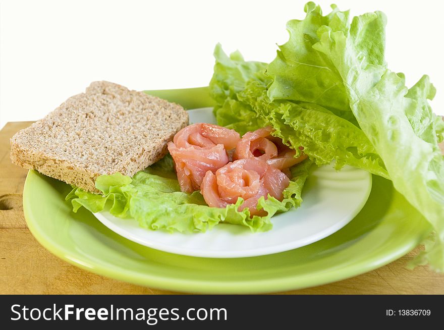 Salmon, bread and salad leaves on a white plate