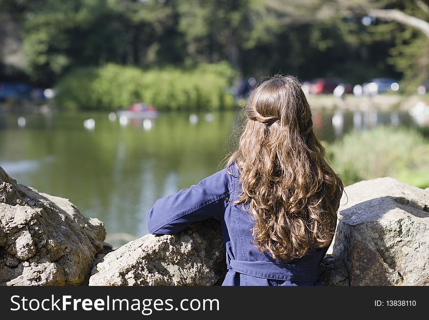 Back of a Woman With Long Brown Hair Looking Over Rocks at a Pond. Back of a Woman With Long Brown Hair Looking Over Rocks at a Pond