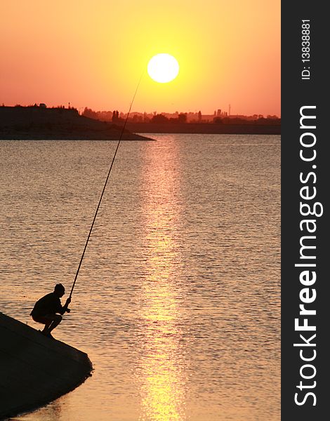 A fisherman throwing his bait in the lake when the sun is about to set. A fisherman throwing his bait in the lake when the sun is about to set