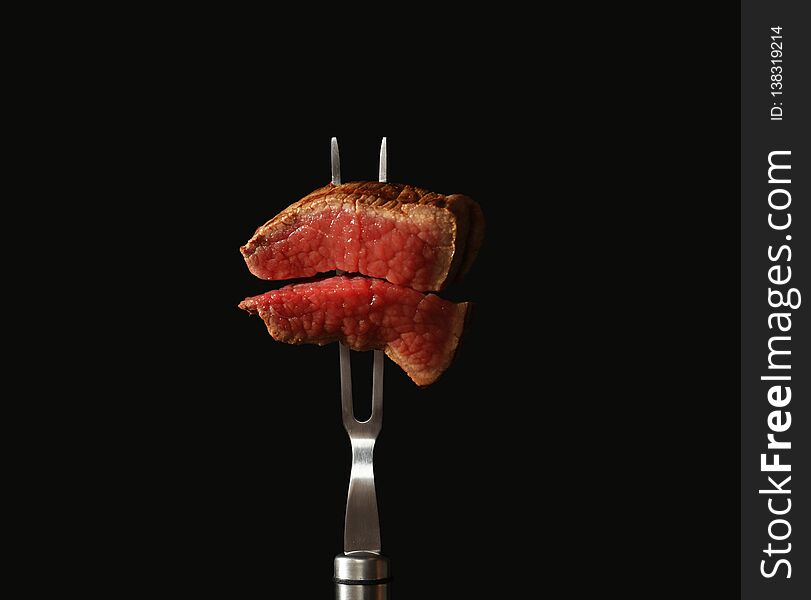 Carving fork with pieces of steak on black background.