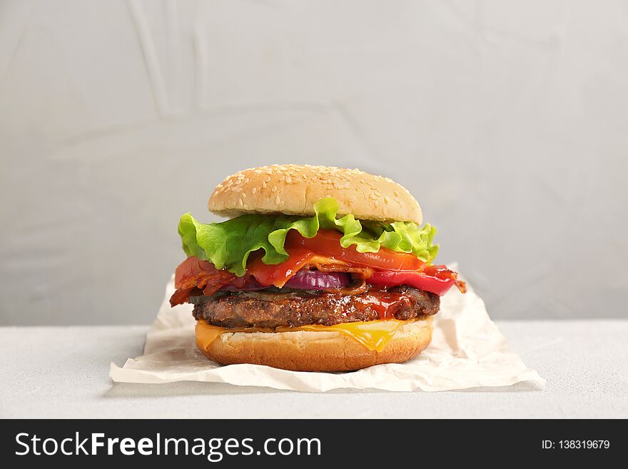 Tasty burger with bacon on table against grey background